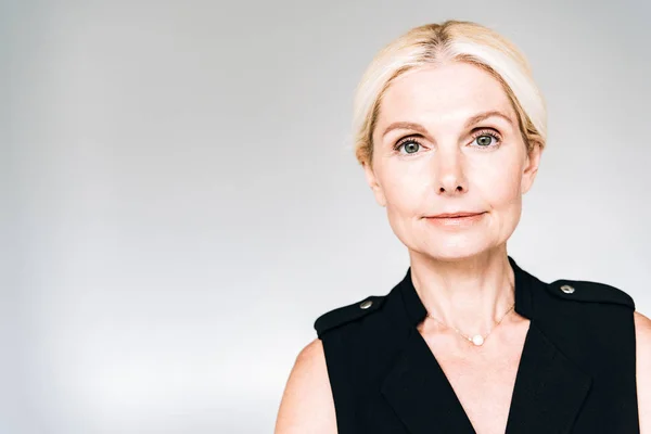 Sonriente elegante mujer madura en traje negro aislado en gris - foto de stock