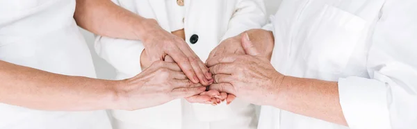 Panoramic shot of cropped view of three generation women in white clothes holding hands isolated on grey — Stock Photo
