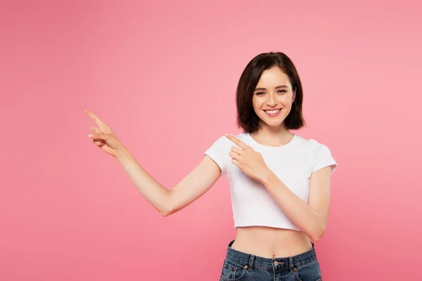 Schöne lächelnde Mädchen zeigt mit den Fingern zur Seite isoliert auf rosa — Stockfoto