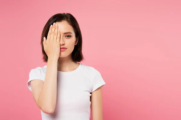 Hermosa chica cubriendo la cara con la mano aislada en rosa - foto de stock