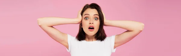 Panoramic shot of beautiful surprised girl with hands on head isolated on pink — Stock Photo
