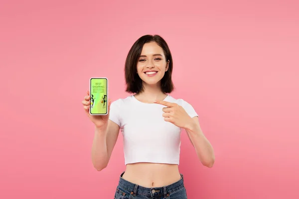 Chica sonriente apuntando con el dedo en el teléfono inteligente con aplicación de compras en línea - foto de stock