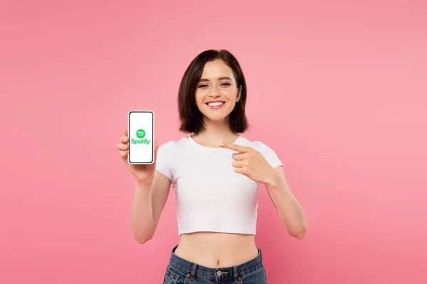 KYIV, UKRAINE - JULY 3, 2019: smiling girl pointing with finger at smartphone with spotify logo. — Stock Photo