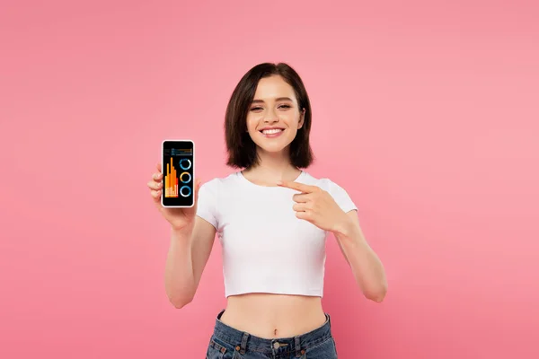 Chica sonriente apuntando con el dedo en el teléfono inteligente con aplicación de análisis de negocios - foto de stock