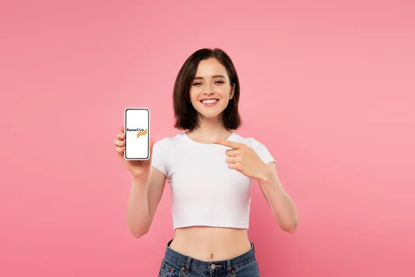 KYIV, UKRAINE - 3 de julho de 2019: menina sorridente apontando com o dedo para o smartphone com o logotipo do clube Forex isolado no rosa — Fotografia de Stock