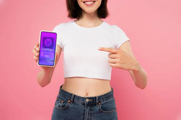 Recortado vista de chica apuntando con el dedo en el teléfono inteligente con aplicación de compras aislado en rosa - foto de stock