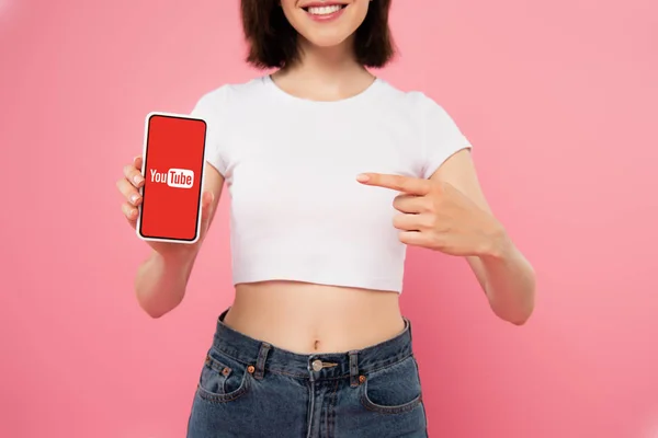 KYIV, UKRAINE - JULY 3, 2019: cropped view of girl pointing with finger at smartphone with youtube logo isolated on pink — Stock Photo
