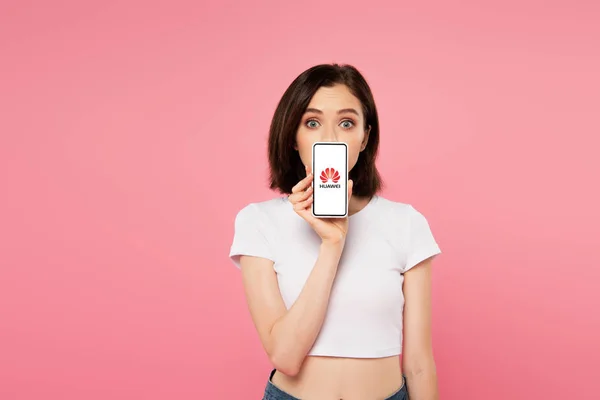 Kyiw, Ukraine - 3. Juli 2019: Schockiertes Mädchen hält Smartphone mit Huawei-Logo isoliert auf rosa — Stockfoto