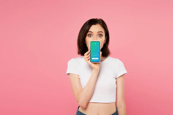 Kyiw, Ukraine - 3. Juli 2019: Schockiertes Mädchen hält Smartphone mit Twitter-Logo isoliert auf rosa — Stockfoto