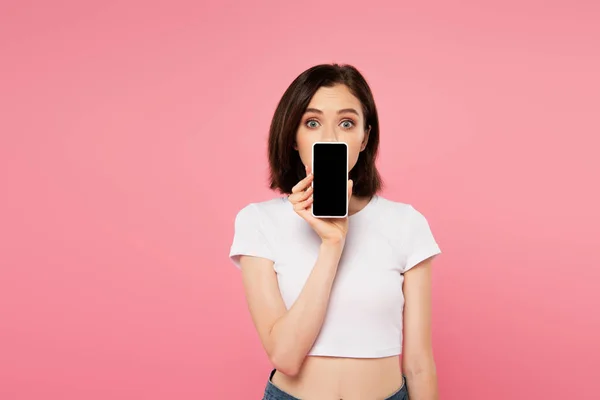 Überraschtes Mädchen hält Smartphone mit leerem Bildschirm auf rosa — Stockfoto