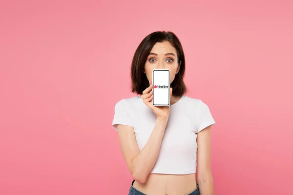 KYIV, UKRAINE - JULHO 3, 2019: menina chocada segurando smartphone com logotipo tinder isolado em rosa — Fotografia de Stock