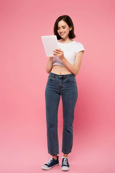 Full length view of beautiful smiling girl using digital tablet isolated on pink — Stock Photo