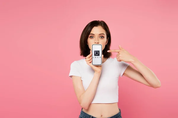 KYIV, UKRAINE - JULY 3, 2019: shocked girl pointing with finger at smartphone with uber logo isolated on pink — Stock Photo