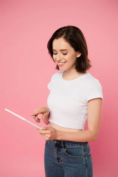 Smiling girl using digital tablet isolated on pink — Stock Photo