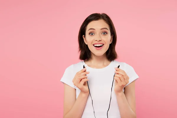 Excitada chica sonriente sosteniendo auriculares aislados en rosa - foto de stock