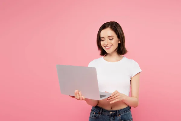 Sorridente bella ragazza utilizzando computer portatile isolato su rosa — Foto stock