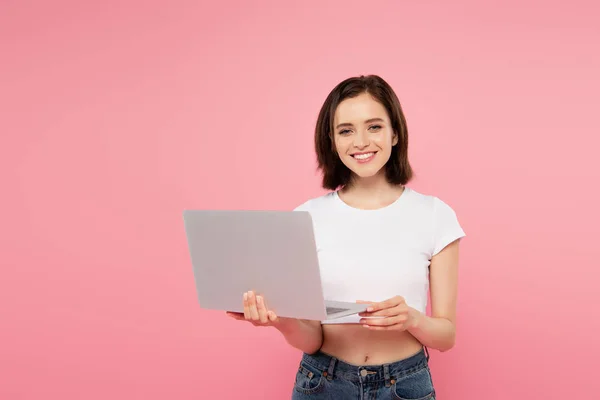 Усміхнена красива дівчина тримає ноутбук ізольовано на рожевому — стокове фото