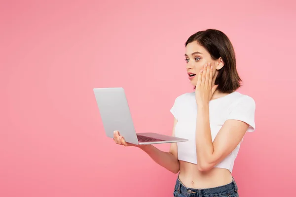 Shocked pretty girl using laptop isolated on pink — Stock Photo