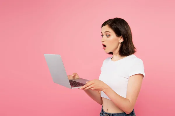 Surprised pretty girl using laptop isolated on pink — Stock Photo