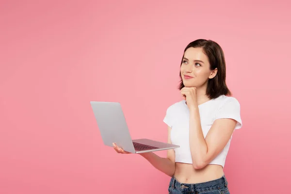 Rêveuse souriante jolie fille en utilisant ordinateur portable isolé sur rose — Photo de stock