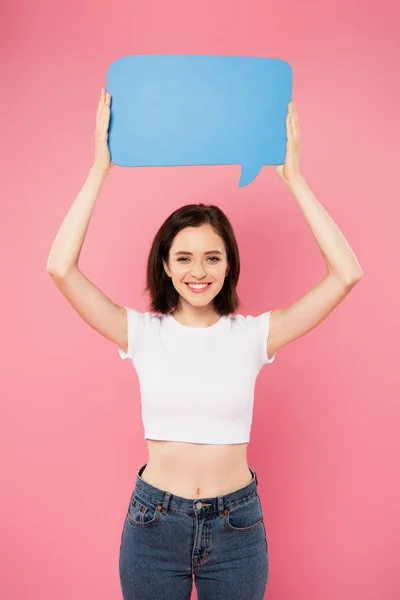 Smiling pretty girl holding blank blue speech bubble isolated on pink — Stock Photo