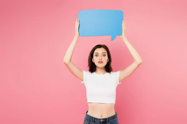 Surprised pretty girl holding blank blue speech bubble isolated on pink — Stock Photo