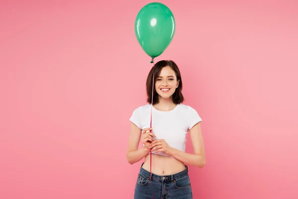 Sonriente bonita chica sosteniendo verde globo aislado en rosa - foto de stock