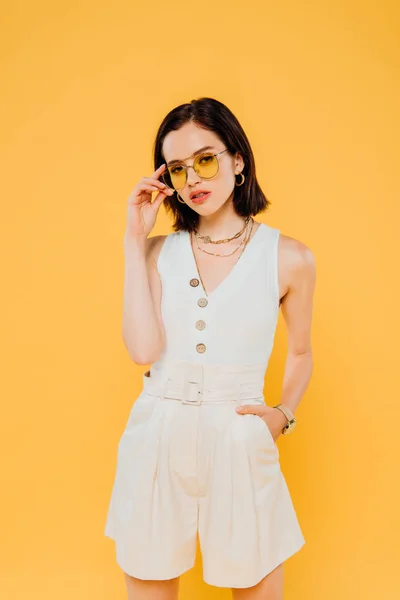 Stylish woman in sunglasses posing with hand in pocket isolated on yellow — Stock Photo