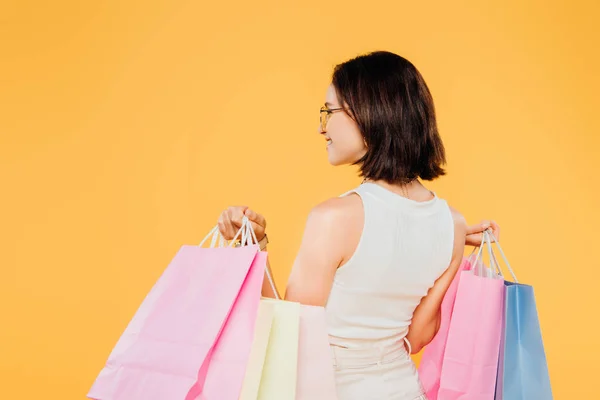 Visão traseira da mulher em óculos de sol segurando sacos de compras isolados no amarelo — Fotografia de Stock