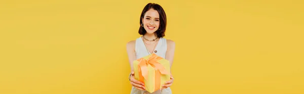 Панорамный снимок счастливой улыбающейся девушки с подарочной коробкой, изолированной на желтый — стоковое фото