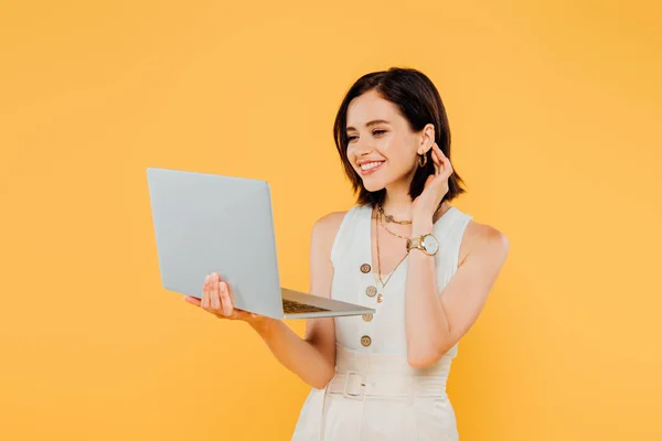 Smiling elegant girl with laptop isolated on yellow — Stock Photo