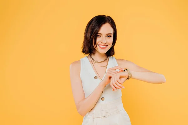 Smiling elegant girl checking time on wristwatch isolated on yellow — Stock Photo