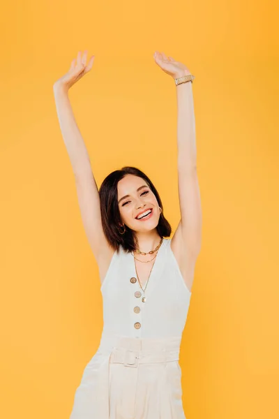 Smiling elegant girl with hands in air isolated on yellow — Stock Photo