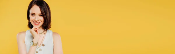 Панорамный снимок улыбающейся элегантной девушки с рукой на подбородке, изолированной на желтом — стоковое фото