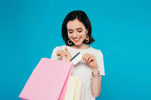 Donna elegante sorridente in abito con borse della spesa in possesso di carta di credito isolata su blu — Foto stock
