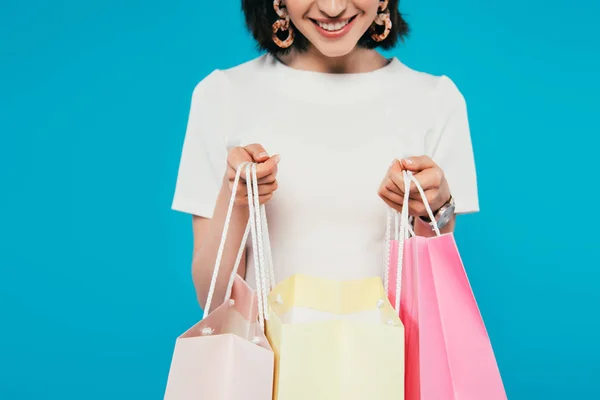 Vista ritagliata di donna elegante sorridente che tiene borse della spesa isolate sul blu — Foto stock