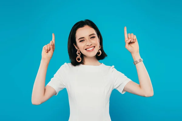 Sonriente mujer elegante en vestido apuntando con los dedos hacia arriba aislado en azul - foto de stock