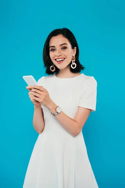 Sonriente mujer elegante en vestido usando teléfono inteligente aislado en azul - foto de stock