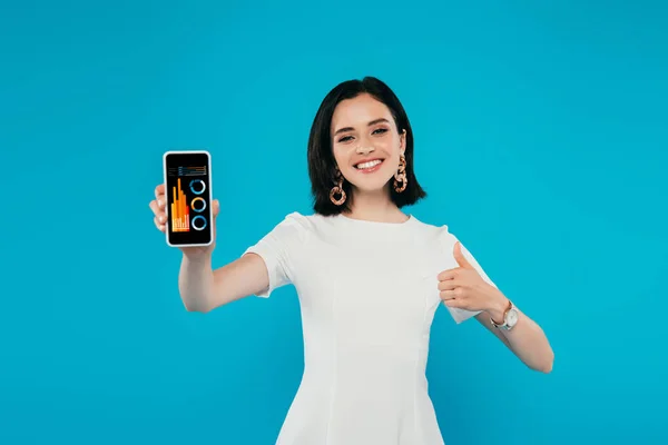 Femme élégante souriante en robe tenant smartphone avec application d'analyse et montrant pouce vers le haut isolé sur bleu — Photo de stock