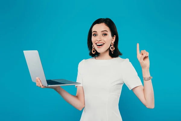 Aufgeregtes Lächeln elegante Frau hält Laptop und zeigt Idee Geste isoliert auf blau — Stockfoto