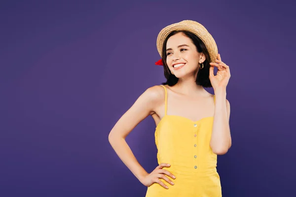 Menina sorridente em chapéu de palha com a mão no quadril olhando para longe isolado em roxo — Fotografia de Stock