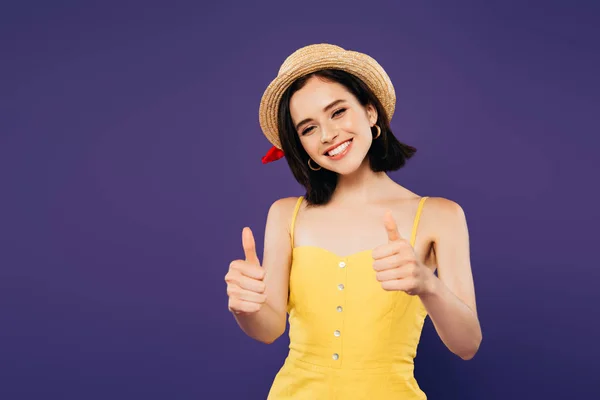 Sonriente chica en sombrero de paja mostrando pulgares hacia arriba aislado en púrpura - foto de stock