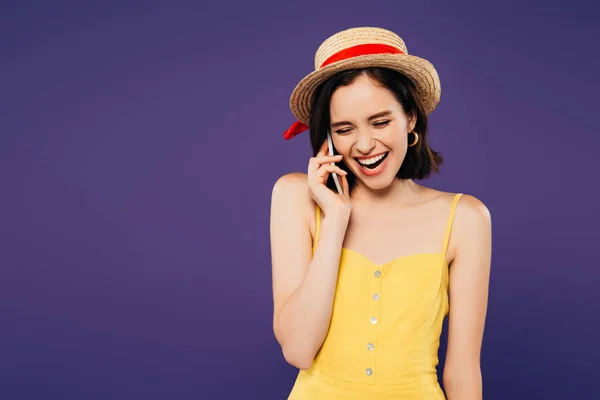 Chica feliz en sombrero de paja hablando en el teléfono inteligente y riendo aislado en púrpura - foto de stock