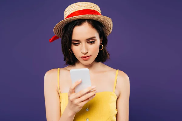 Девушка в соломенной шляпе с помощью смартфона изолированы на фиолетовый — стоковое фото