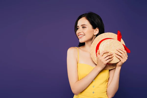 Sorrindo menina bonita segurando chapéu de palha e olhando para longe isolado em roxo — Fotografia de Stock