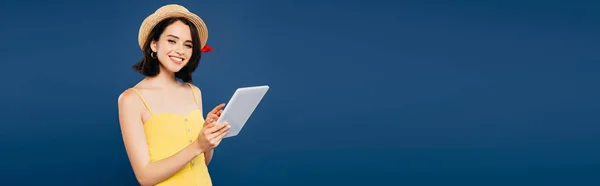 Панорамный снимок улыбающейся красивой девушки в соломенной шляпе, держащей цифровой планшет, изолированный на голубом — стоковое фото