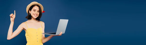 Tiro panorâmico de menina sorridente em chapéu de palha segurando laptop isolado em azul — Fotografia de Stock