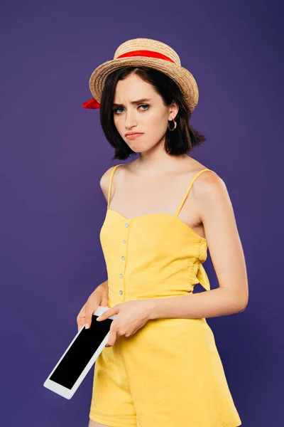 Сумна красива дівчина в солом'яному капелюсі тримає цифровий планшет з порожнім екраном ізольовано на фіолетовому — стокове фото