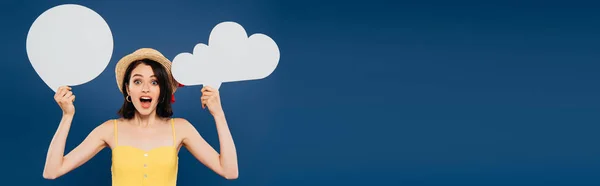 Excited girl in straw hat holding empty white thought and speech bubbles isolated on blue — Stock Photo