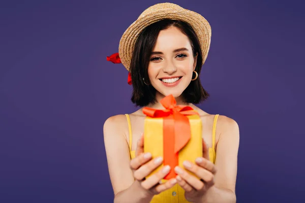 Chica sonriente en sombrero de paja regalo aislado en púrpura - foto de stock